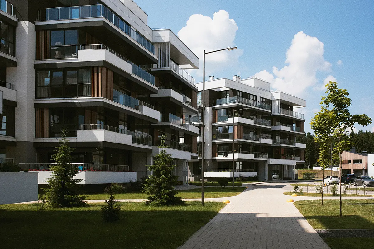 Mehrfamilienhaus bei sonnigem Wetter mit Gehweg Rasen und Bäumen davor